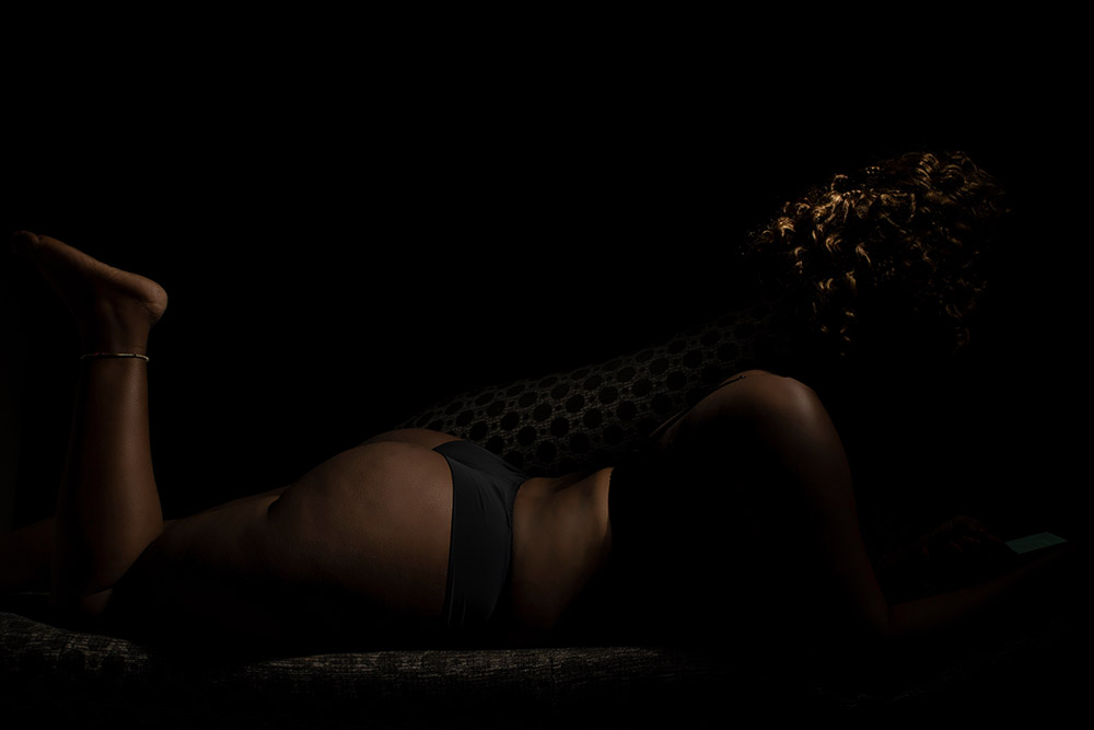 Low-key boudoir photo of a young African woman lying on her side